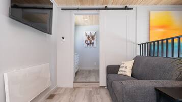 A modern living room with a grey sofa, a TV mounted on the wall, a painting of deer, and a staircase with a railing.