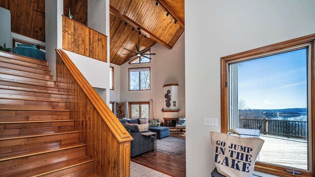 A spacious living area with a wooden staircase, a large window overlooking a lake, and a sign reading "GO JUMP IN THE LAKE". - Available Labor Day Wkd, Lake Front, Pickleball! (Garfield)