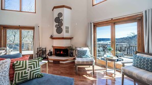 A spacious living room with a fireplace, large windows, and a balcony with outdoor seating. - Available Labor Day Wkd, Lake Front, Pickleball! (Garfield)