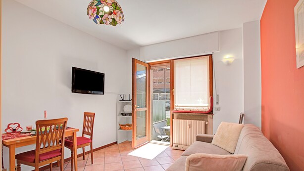 A living room with a sofa, a TV mounted on the wall, a dining table with chairs, and a sliding glass door leading to an outdoor area. - Bardonest - Central Studio in Bardonecchia (Bardonecchia)