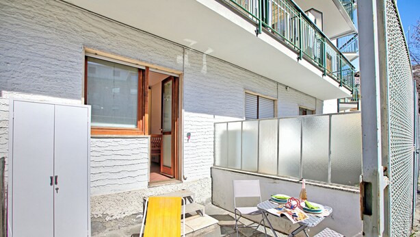 A residential building with a balcony, a wooden door, a white wall, and a table with a chair. - Bardonest - Central Studio in Bardonecchia (Bardonecchia)