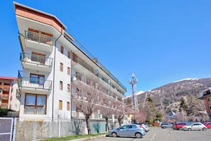 A multi-story building with balconies, a parking lot, and a mountainous backdrop. - Bardonest - Central Apartment in Bardonecchia (Bardonecchia)