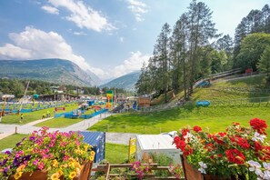 Paesaggio montuoso con cielo sereno, area campeggio segnalata e cartello con la scritta 'Summer Camp'.
