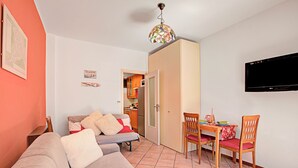 A living room with a sofa, a dining table with chairs, a television, and a kitchen in the background. - Bardonest - Central Studio in Bardonecchia (Bardonecchia)