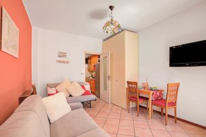 A living room with a sofa, a dining table with chairs, a television, and a kitchen in the background. - Bardonest - Central Apartment in Bardonecchia (Bardonecchia)