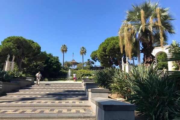 A grand staircase leading to a building with classical architecture, surrounded by lush greenery and palm trees.