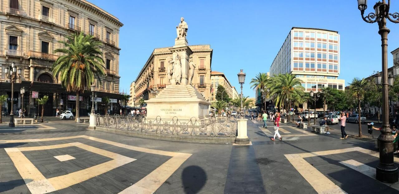 A public square with a central monument, surrounding buildings, and palm trees.