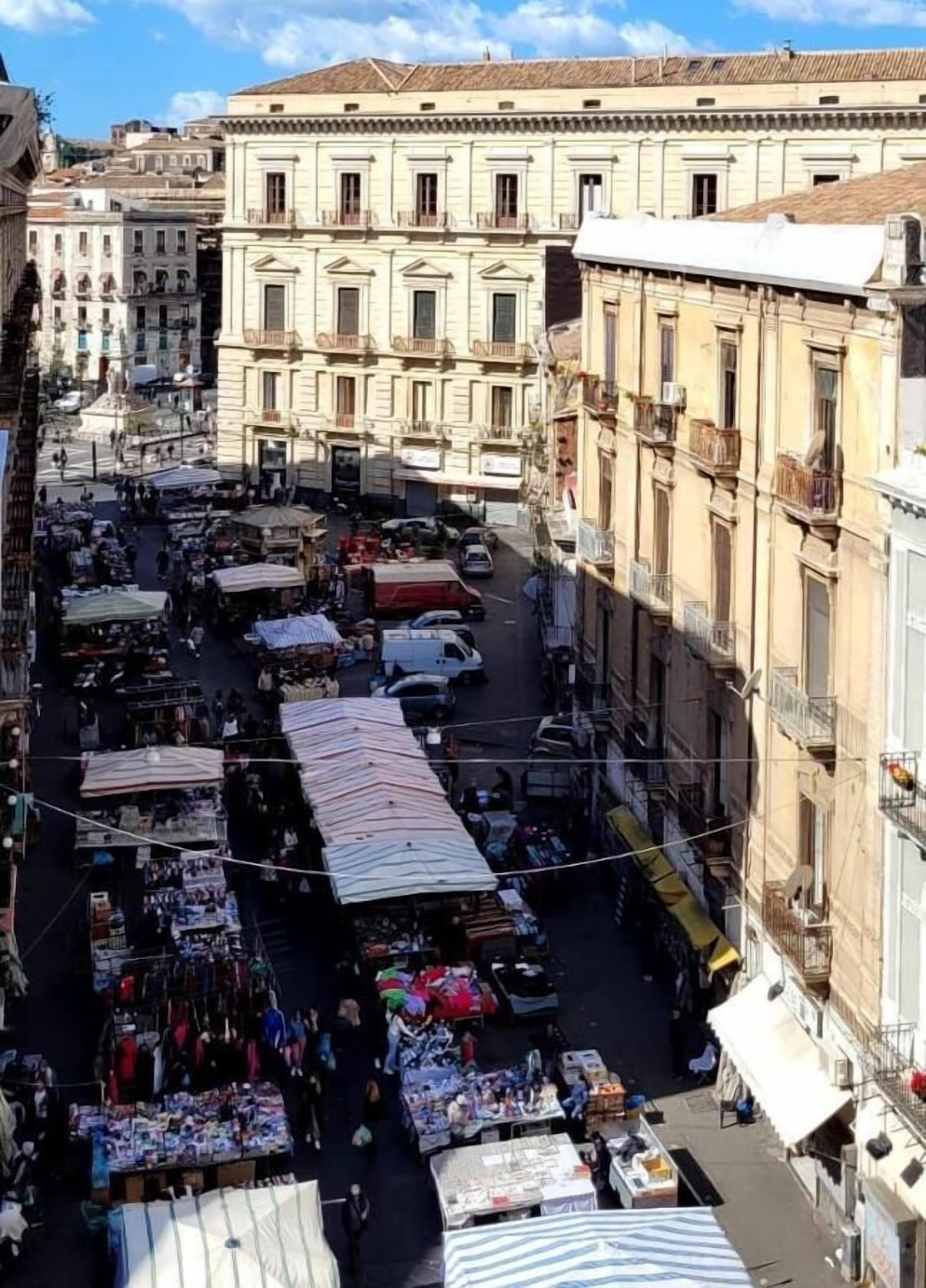 A bustling street market with vendors and stalls, surrounded by historic buildings with classical architecture.