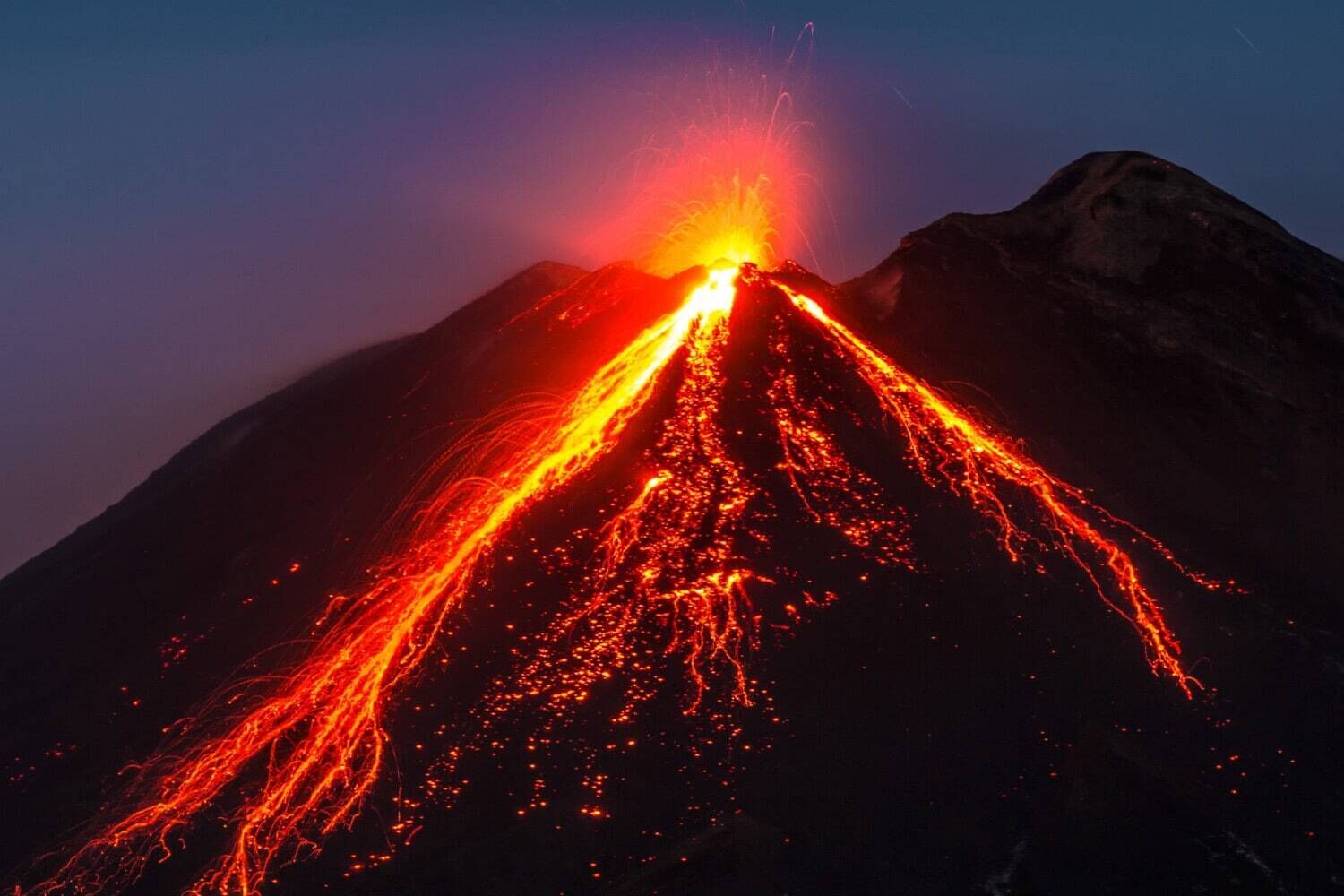 A volcano erupting at night with lava flowing down its sides.