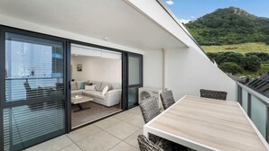 En moderne balkon med spisebord og fletstole, med udsigt over et frodigt, grønt landskab.