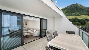 Ein moderner Balkon mit Esstisch und Korbstühlen, mit Blick auf eine üppige grüne Landschaft.