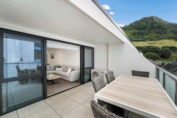 A modern balcony with a dining table and wicker chairs, overlooking a lush green landscape.