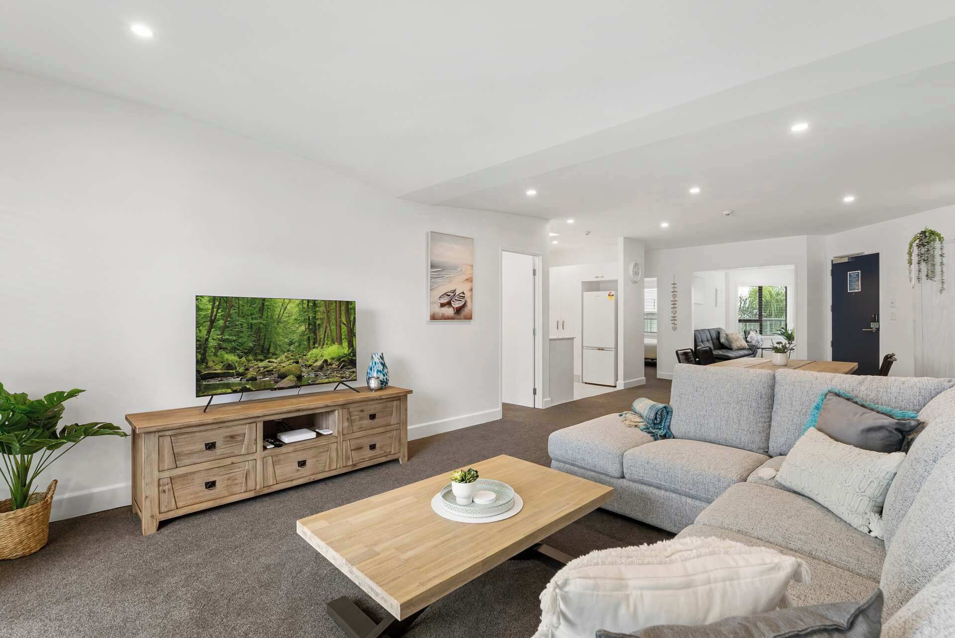 A modern living room with a large flat-screen TV, a wooden entertainment unit, a grey sofa, and a coffee table.