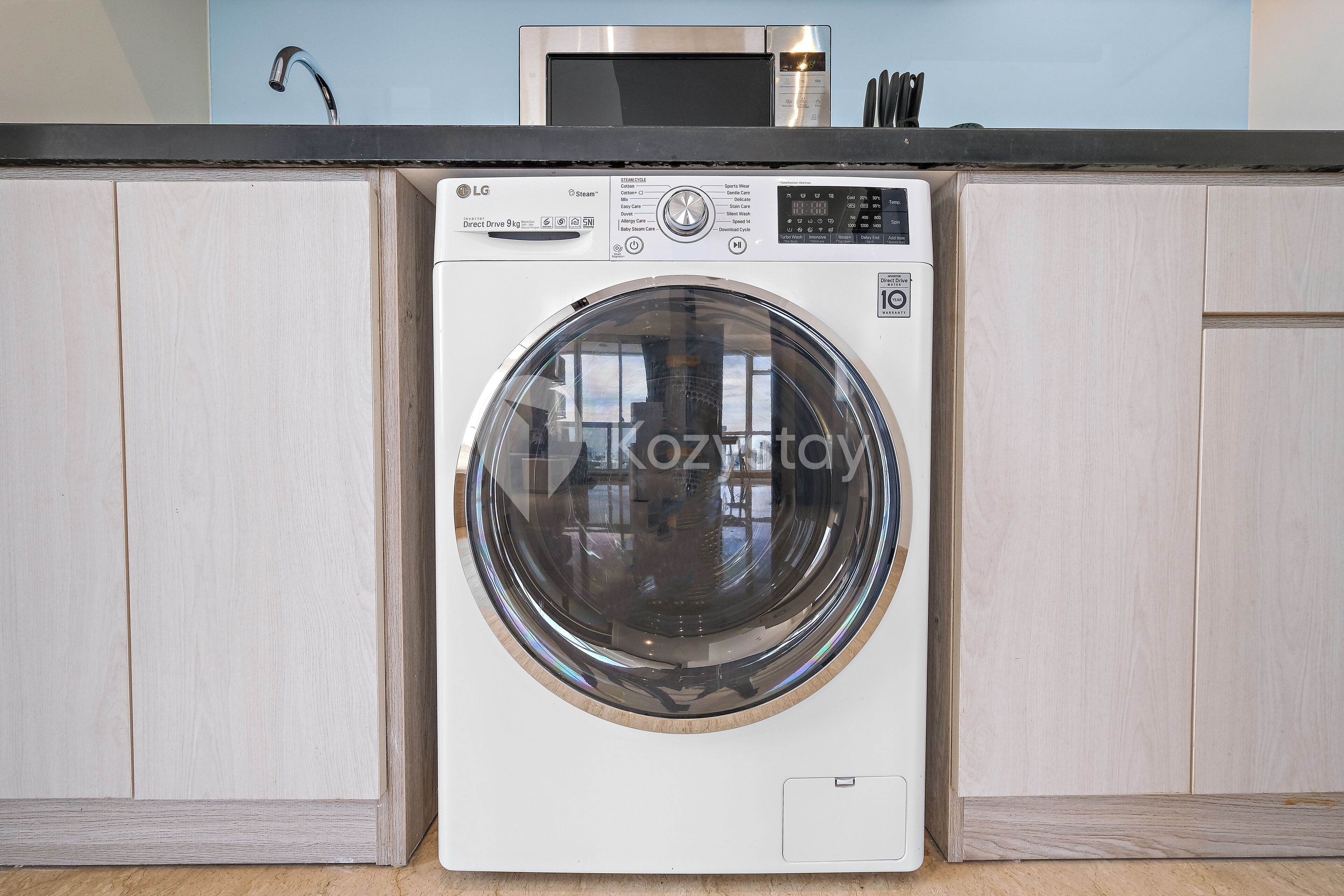 A front-loading washing machine in a kitchen with wooden cabinets and a countertop.