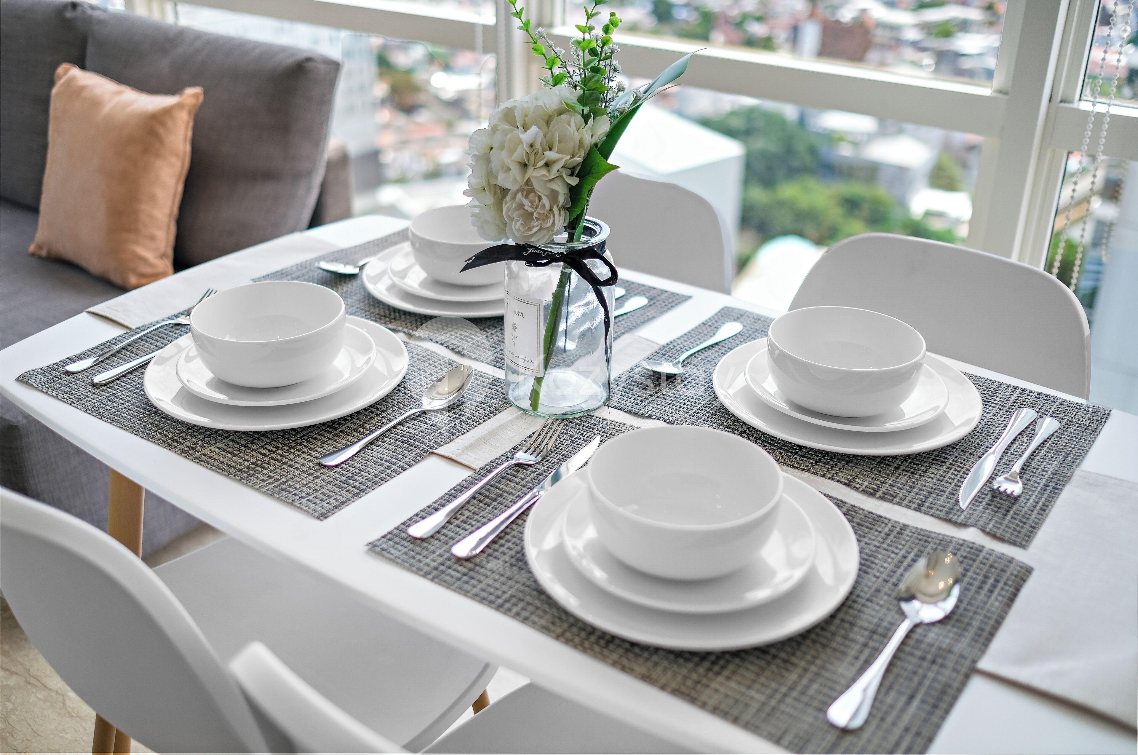 A dining table set with white plates, silverware, and a vase with white flowers.