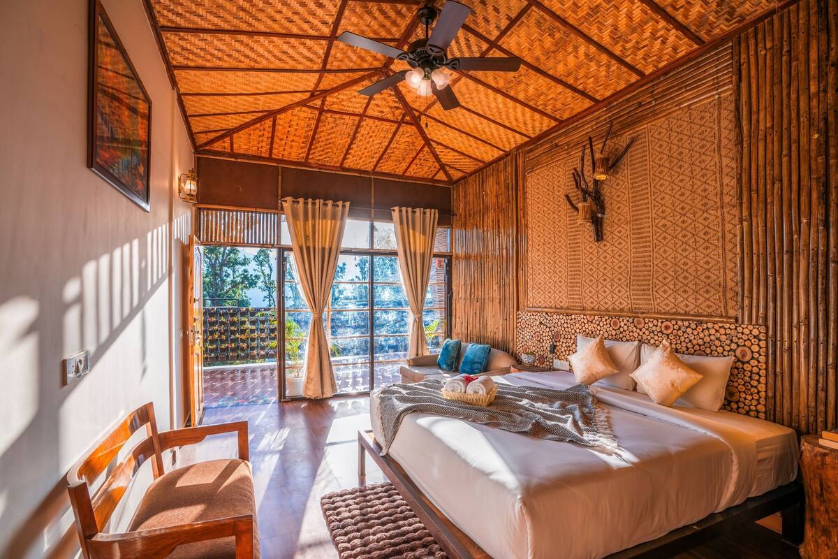 A bedroom with a bed, a wooden chair, a ceiling fan, and a large window with curtains.