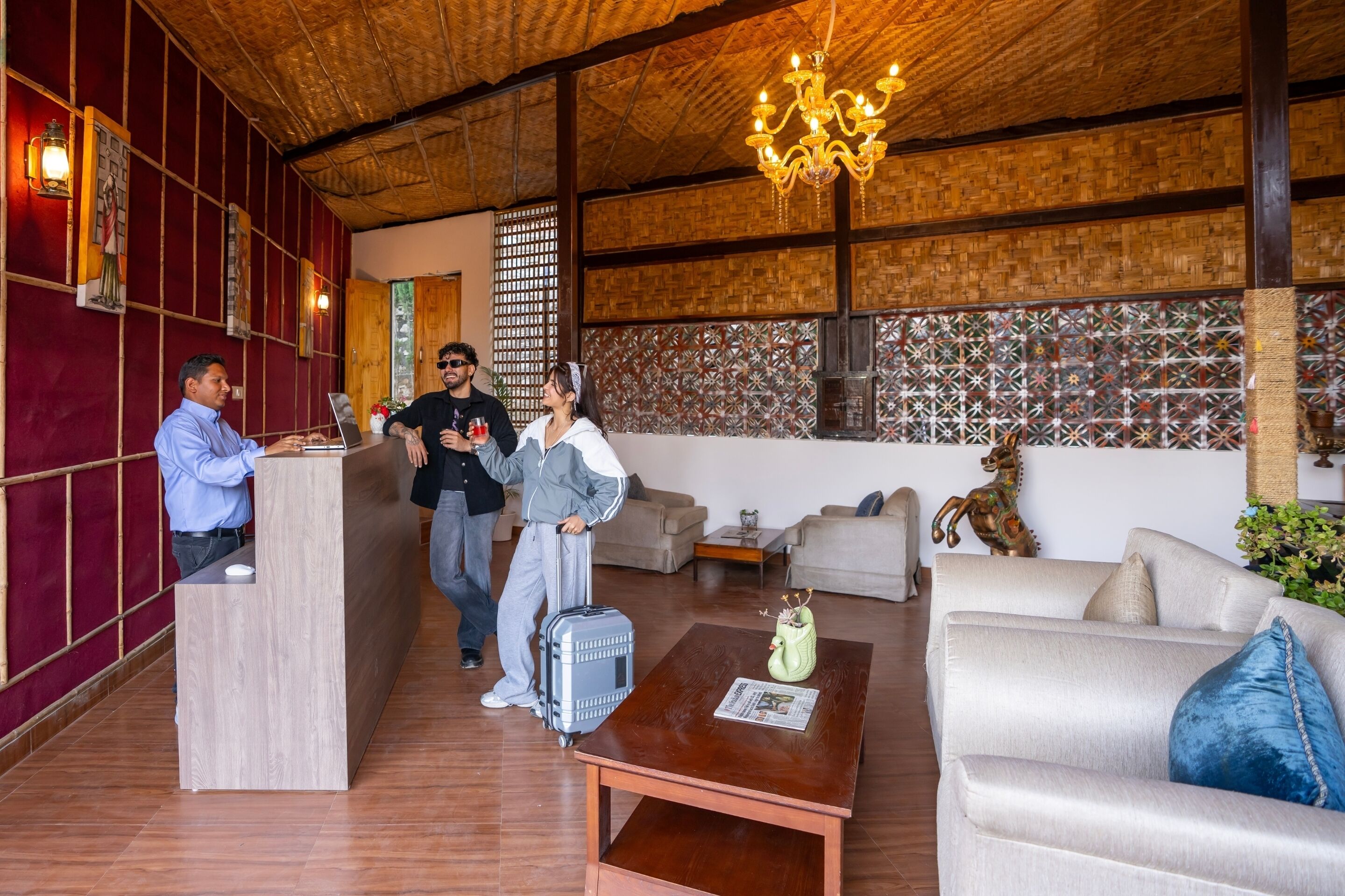 A reception area with a wooden reception desk, a chandelier, and a patterned wall. There are sofas and a coffee table in the living area.
