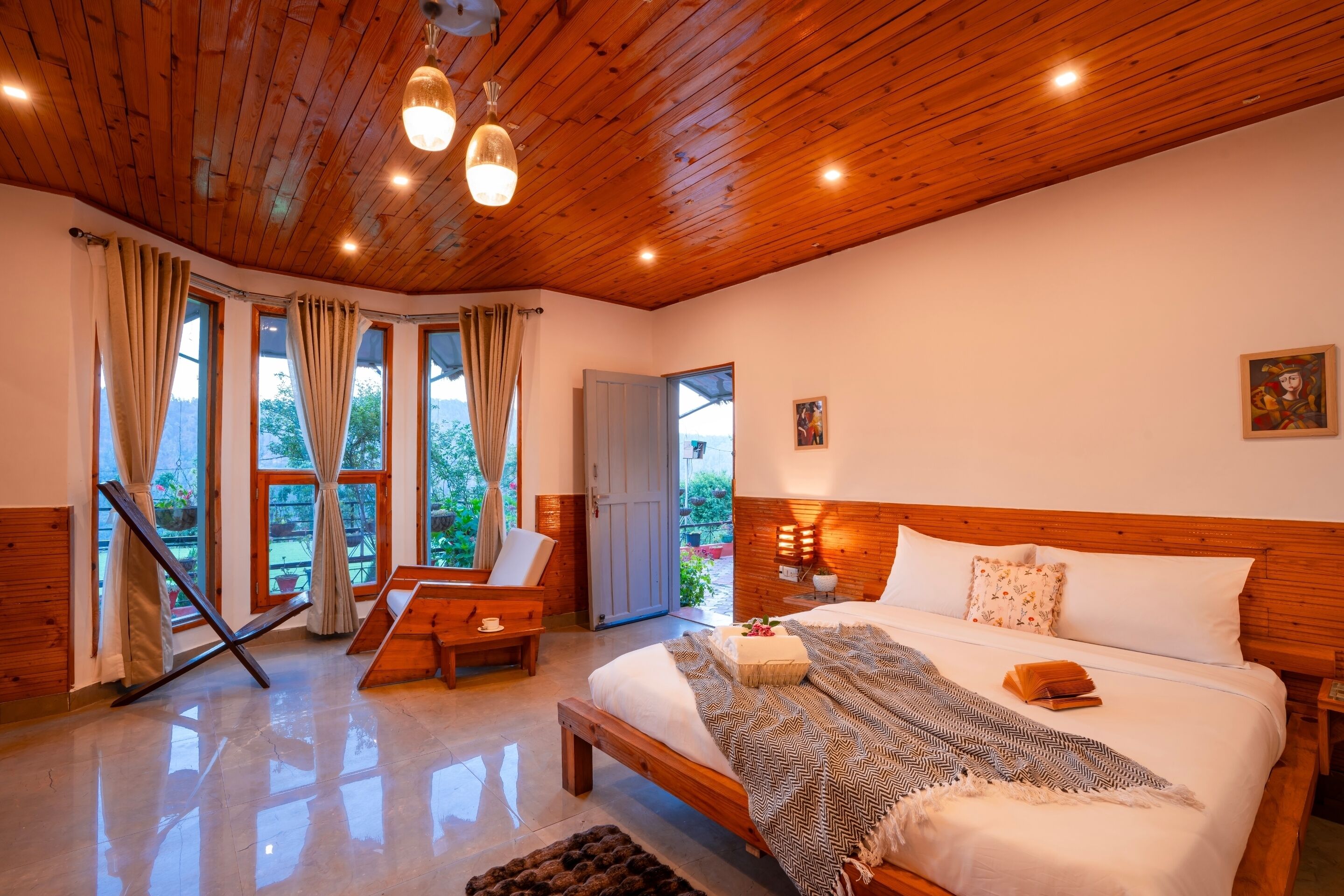 Une chambre spacieuse avec un plafond en bois, de grandes fenêtres, un lit recouvert d’une couverture à motifs et un banc en bois.
