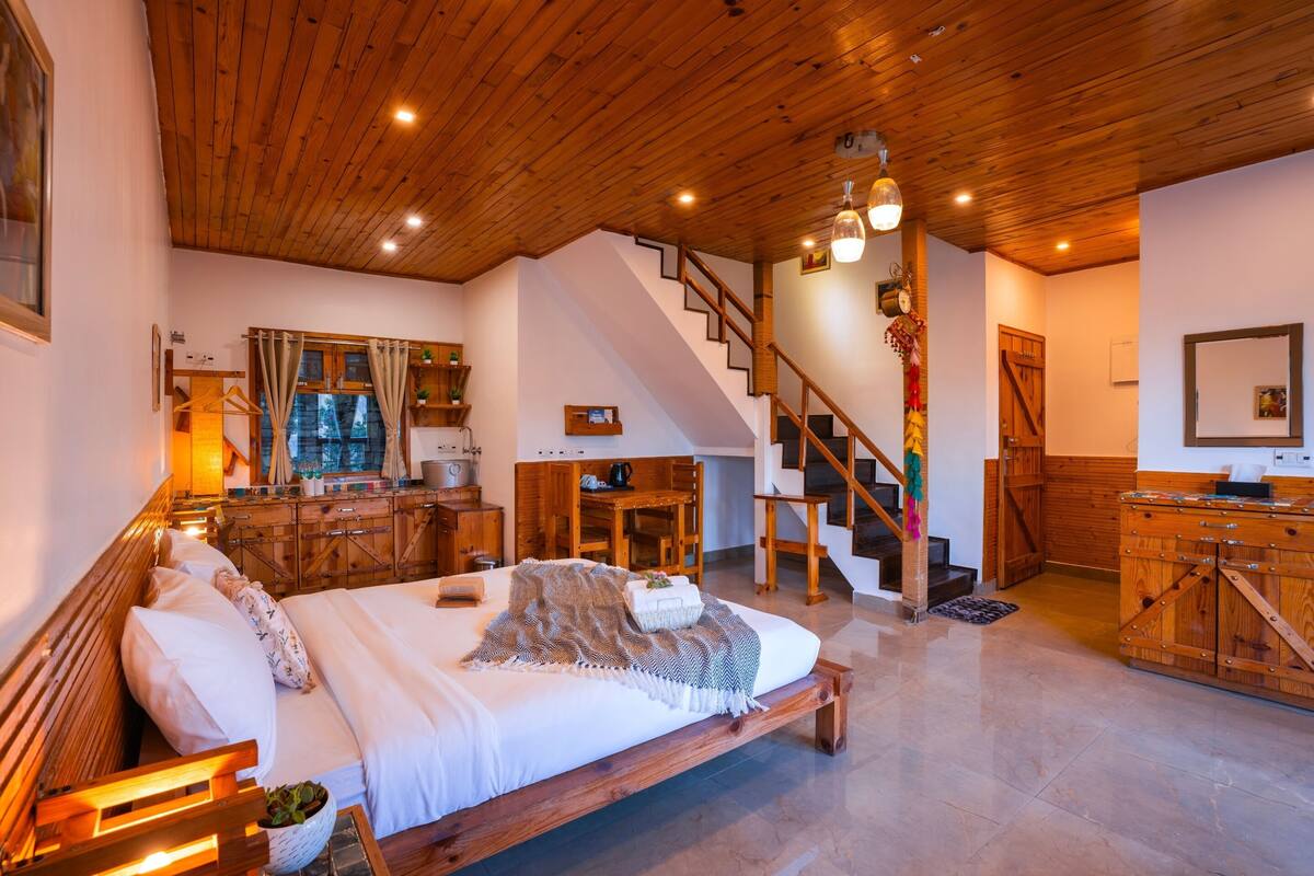A spacious bedroom with a large bed, wooden ceiling, and a staircase leading to an upper level.