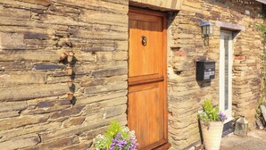 Edifici de pedra amb una porta de fusta, una bústia i testos amb flors a terra.