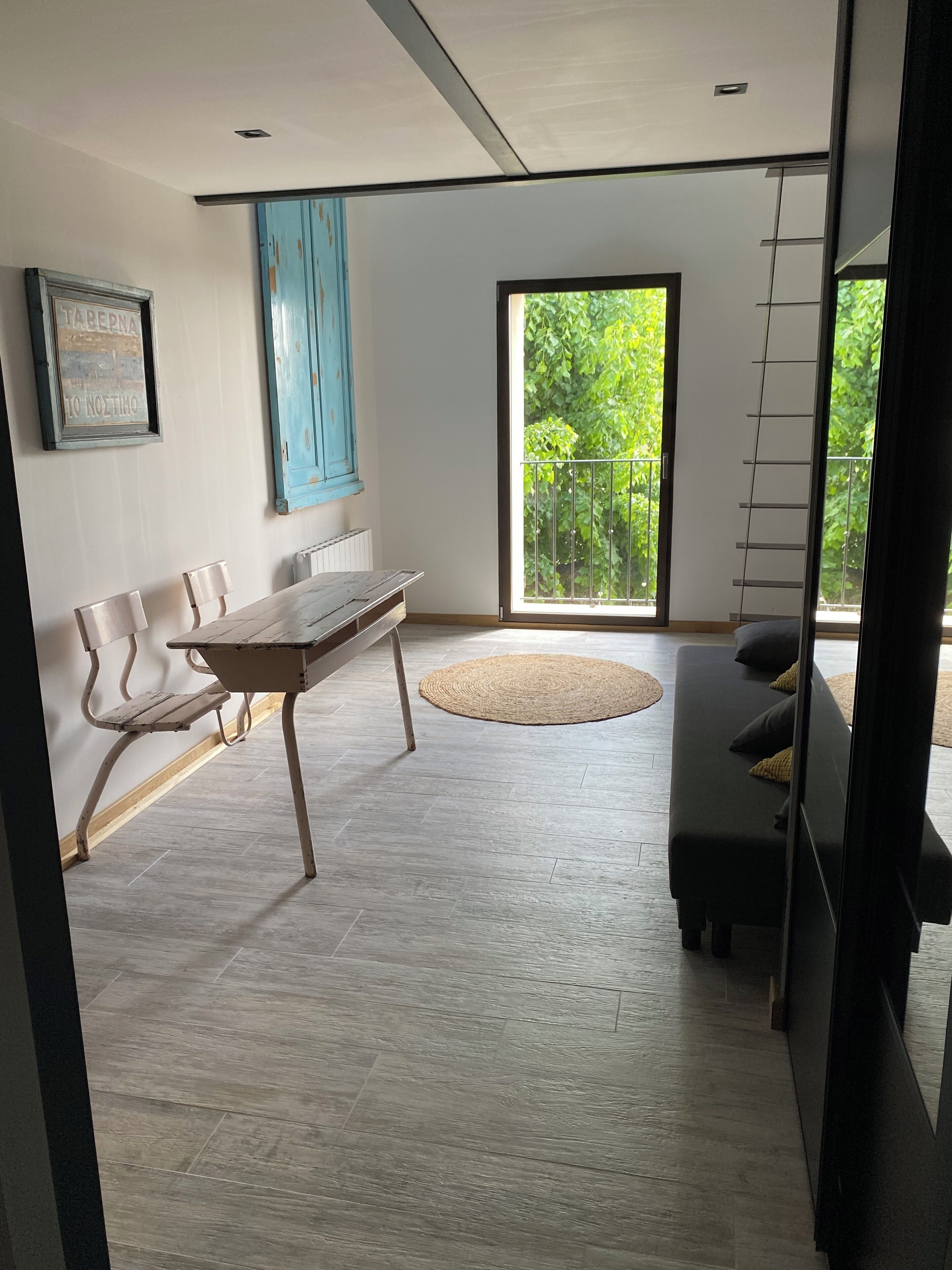 A modern room with a dining table, chairs, a sofa, and a large window with a view of greenery.
