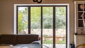A living room with a sofa, a table, and a sliding glass door leading to an outdoor area with a stone wall and greenery. - Coudignac 1891 (Lagnes)