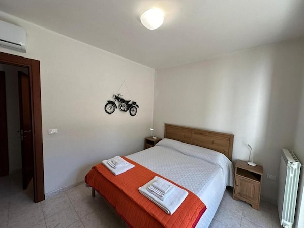 A bedroom with a bed, a nightstand, a radiator, and a motorcycle decoration on the wall. - Room-andromeda Rooms Otranto (Otranto)