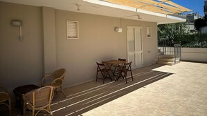 Un espacio al aire libre techado con una mesa, sillas, una puerta y un ventanal pequeño.