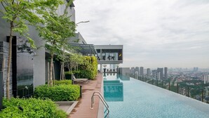A modern building with a rooftop infinity pool, lush greenery, and a city view.