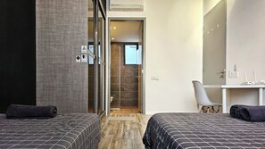 A hotel room with two beds, a desk, a chair, a shower, and a toilet.