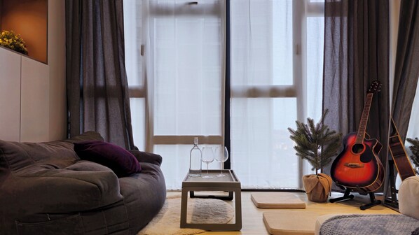 A cozy living room with a grey sofa, a small coffee table, a guitar, and a Christmas tree.