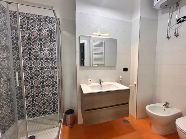 Un baño con ducha, lavamanos con espejo, un bidé y un inodoro.