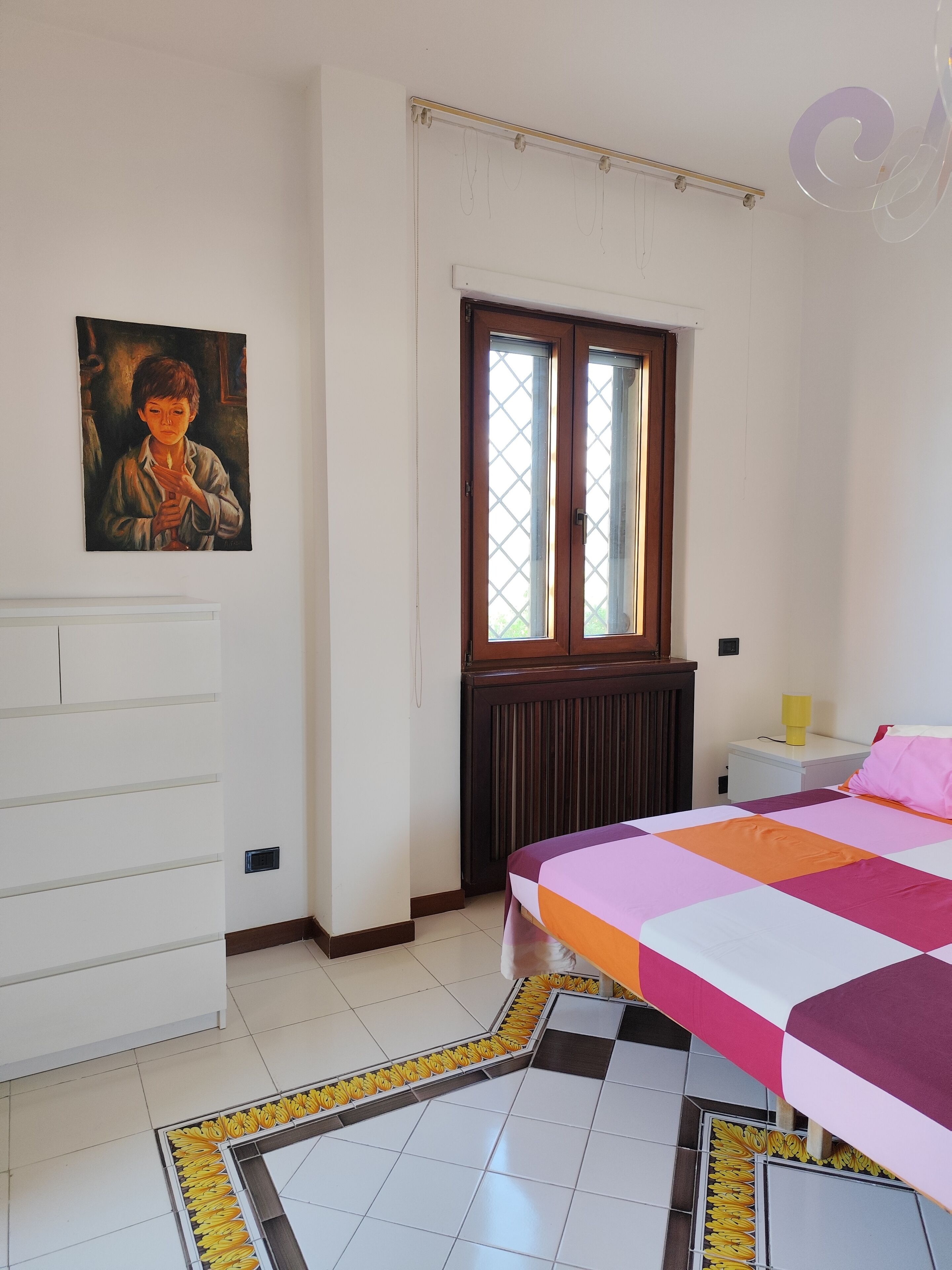 Ein Schlafzimmer mit Bett, Nachttisch, Schminktisch, Fenster mit Jalousien und einem Bild an der Wand.