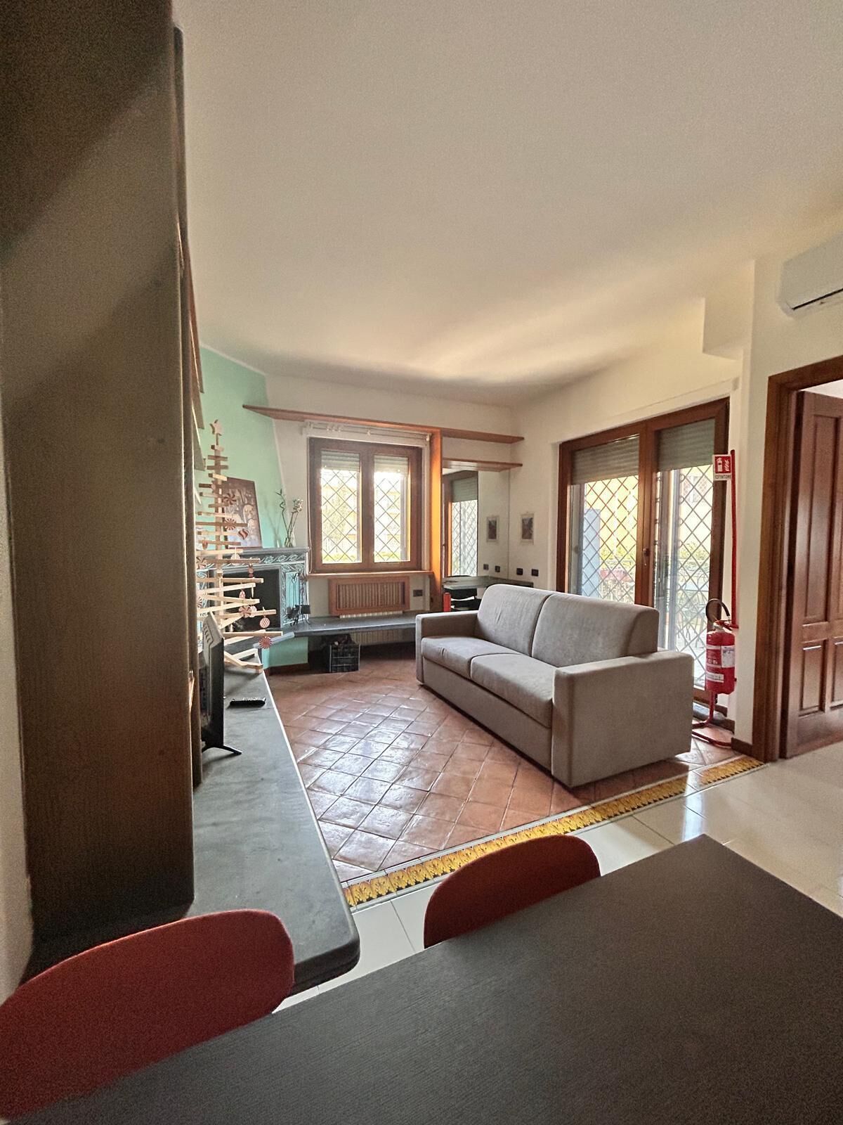 Ein Wohnzimmer mit Sofa, einem Esstisch mit Stühlen, einer Küchenzeile inklusive Herd und einem Fenster mit Ausblick.