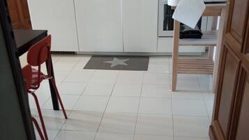Eine Küche mit weißen Schränken, einer gefliesten Spritzschutzwand, einer Waage und einem Stuhl.