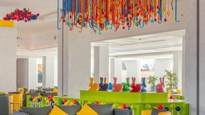 Eine moderne Lobby mit einem farbenfrohen Kronleuchter, einem grünen Empfangstresen und einer Sitzecke mit gelben und grauen Sofas.