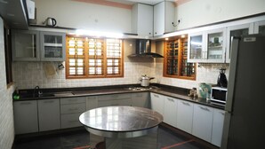 A kitchen with white cabinets, a round glass table, a stove, and a refrigerator. - Sugandhi Bhoja Shetty (Mangaluru)