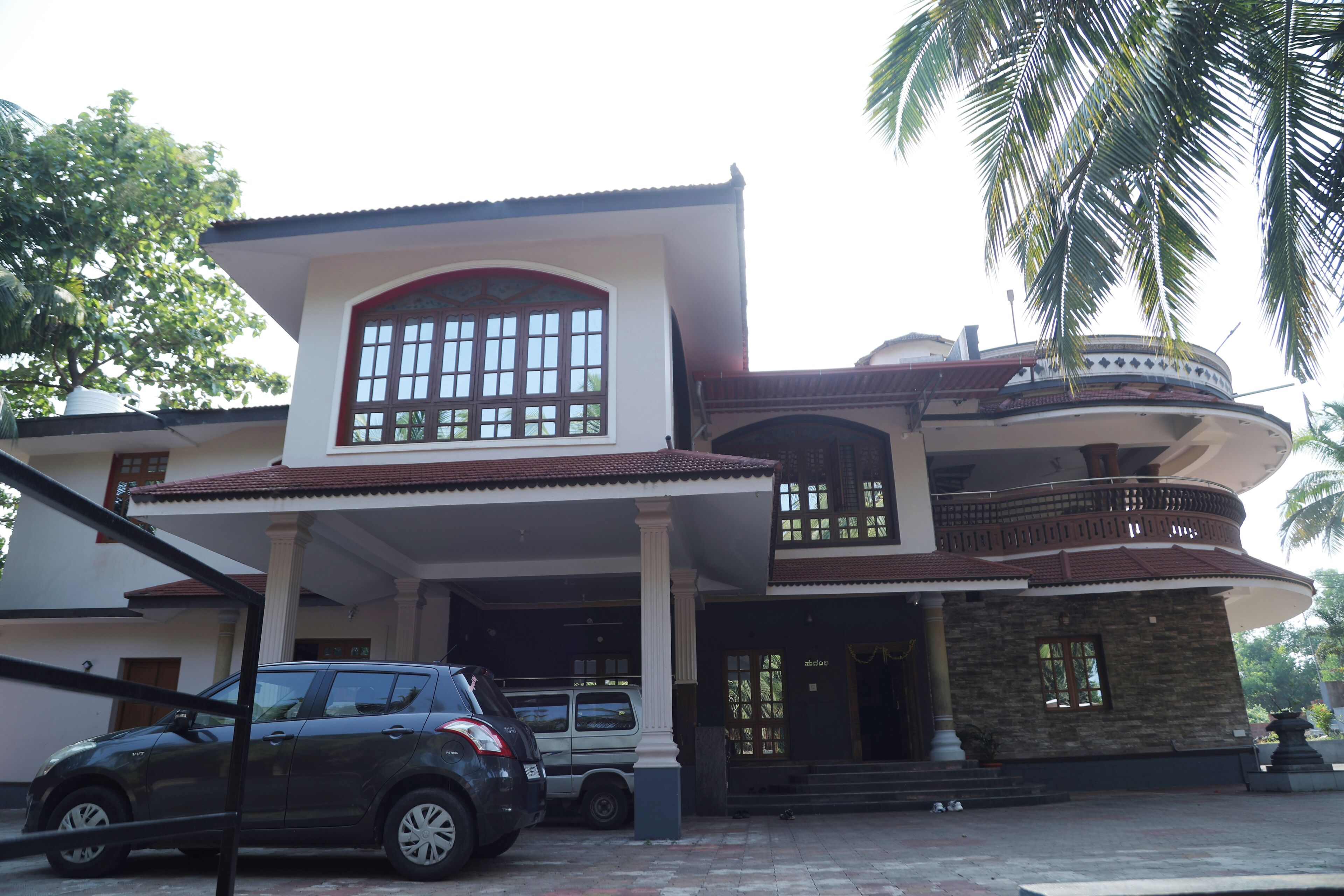 A two-story house with a balcony, a car parked in front, and a palm tree.