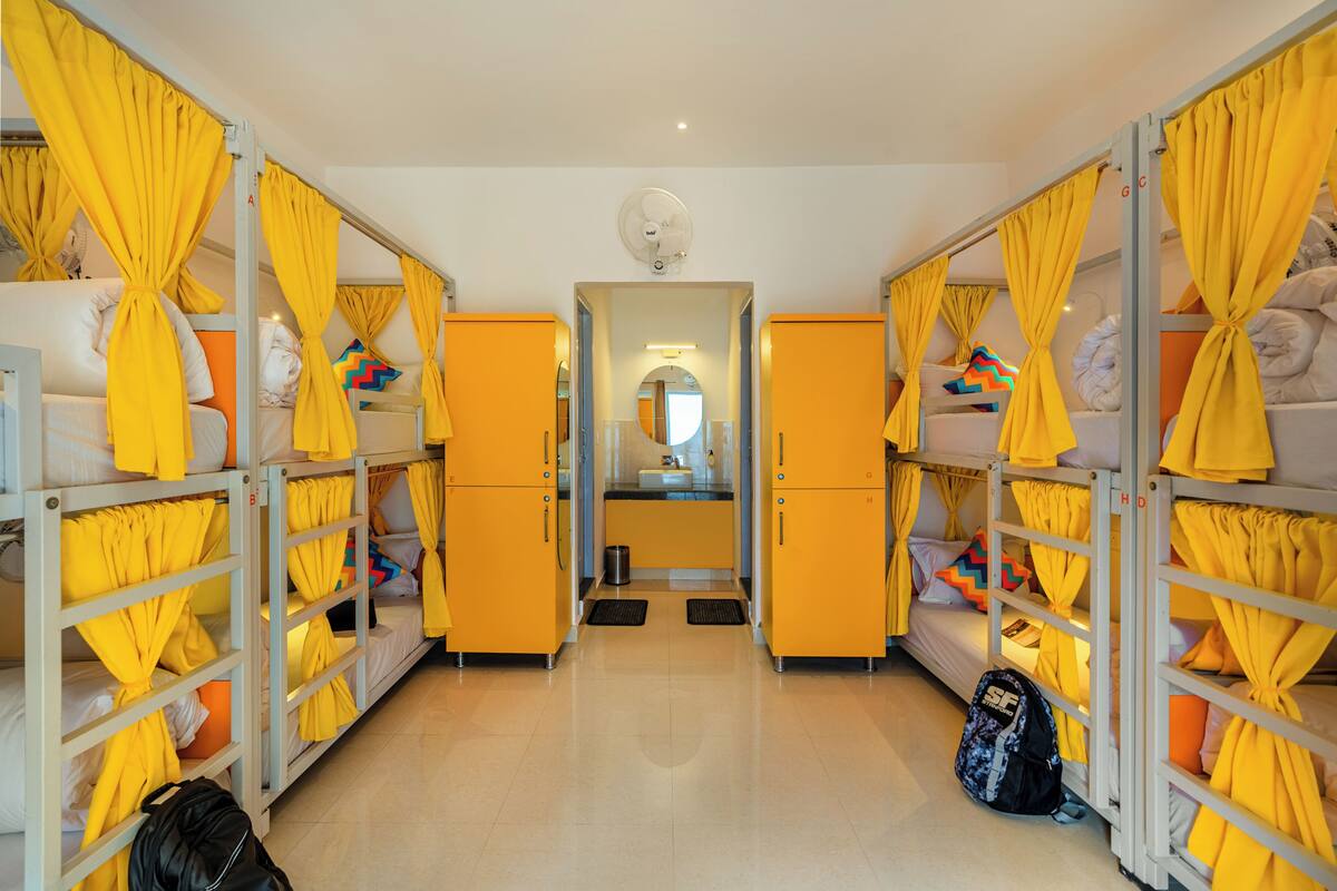 A hotel room with bunk beds, yellow curtains, a mirror, and a fan.