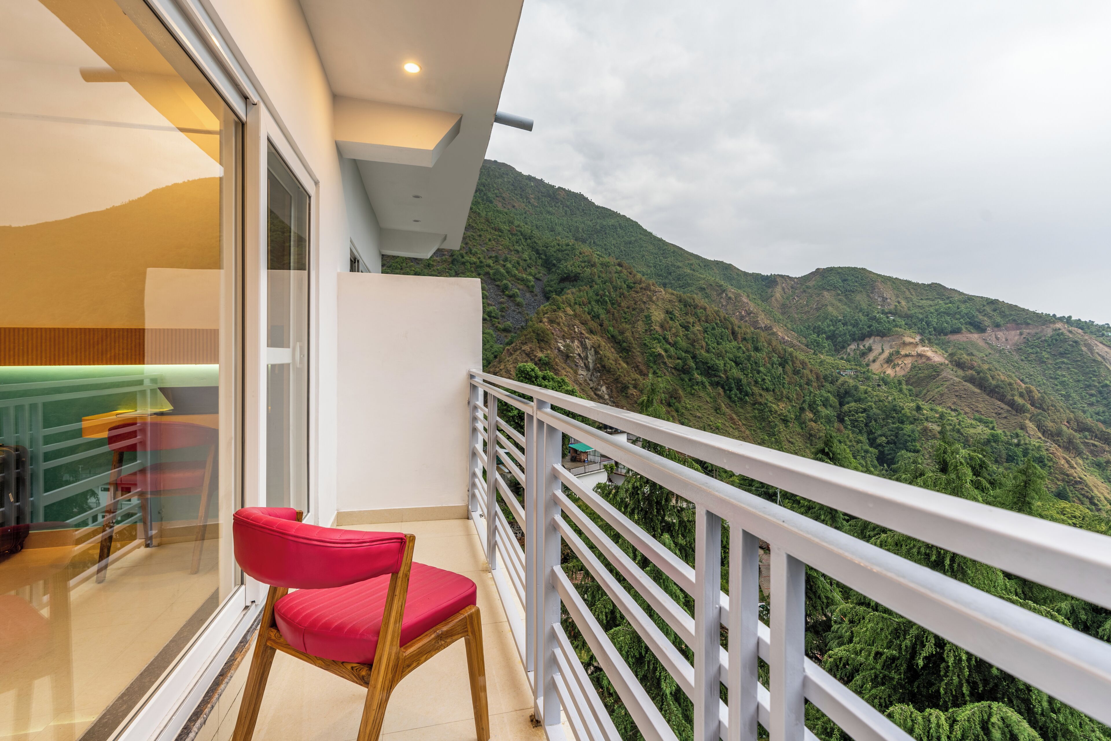 A balcony with a red chair, a glass door leading to a room, and a view of a mountainous landscape.