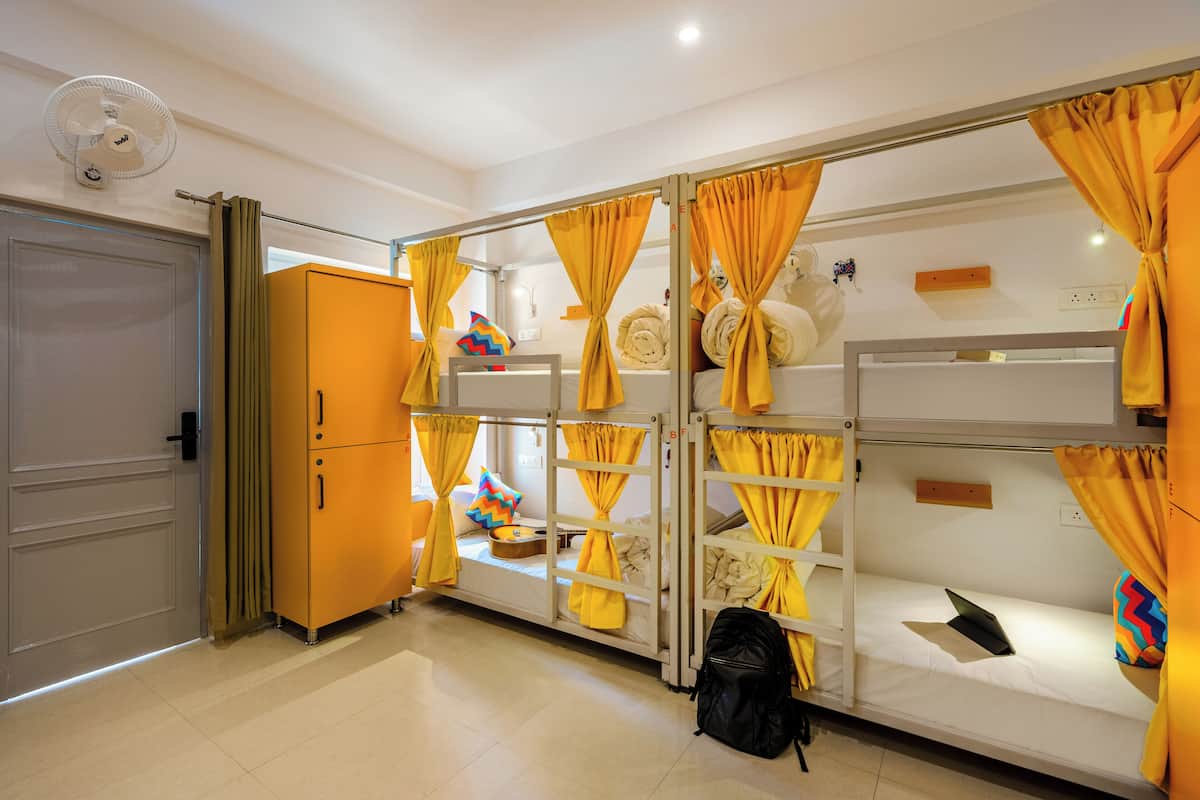 A dormitory room with bunk beds, a wardrobe, and a fan.