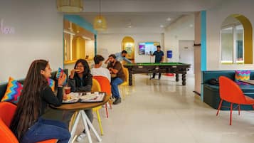 A 24/7 in-house cafe with a pool table, seating areas, and a neon sign.