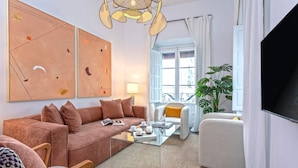 A modern living room with a glass coffee table, a sofa, and a chair. There is a large window with curtains, a plant, and a TV on the wall. - Exclusive Apartment in Seville. Almansa II (Seville)