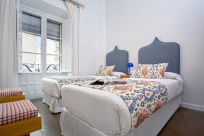A double bed with a patterned bedspread, two bedside tables, a window with blinds, and a view of buildings outside. - Exclusive Apartment in Seville. Almansa II (Seville)