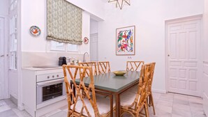 A compact kitchen with white cabinetry, a built-in oven, and a dining area with a green table and wicker chairs. - Exclusive Apartment in Seville. Almansa II (Seville)