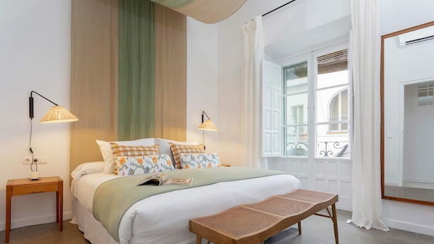A neatly arranged bedroom with a bed, bedside tables, a bench, and a window with a view of a balcony. - Exclusive Apartment in Seville. Almansa II (Seville)