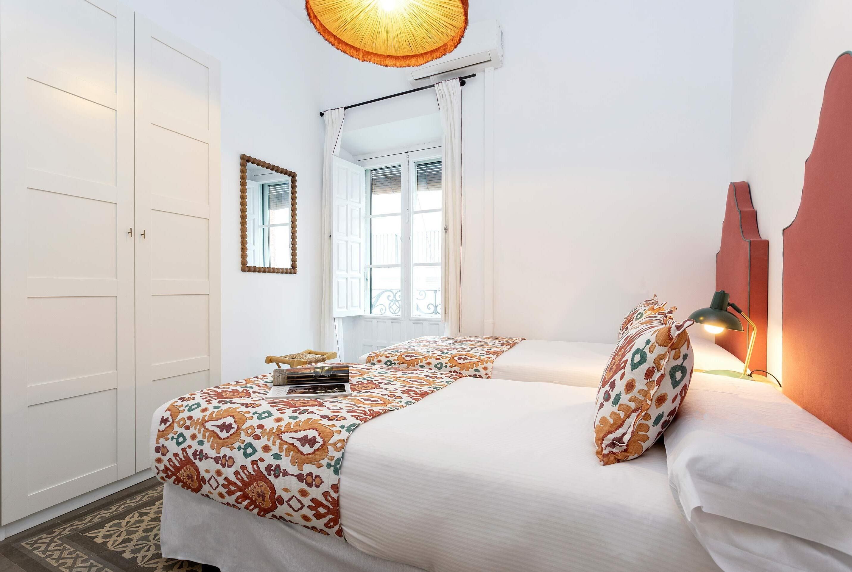 A bedroom with a bed, a mirror, a window, and a lamp.