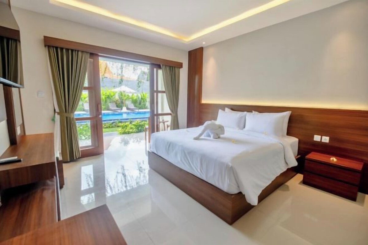 A modern hotel room with a large bed, wooden headboard, and a view of a swimming pool.
