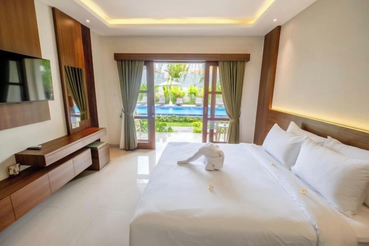 Une chambre d’hôtel avec un grand lit, un téléviseur fixé au mur et une vue sur la piscine depuis la fenêtre.
