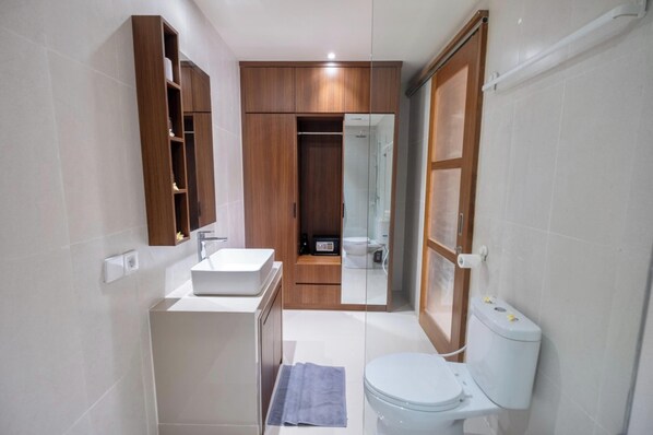 A modern bathroom with a wooden vanity, a toilet, and a glass-enclosed shower. - Puri Kaja House (Tibubeneng)